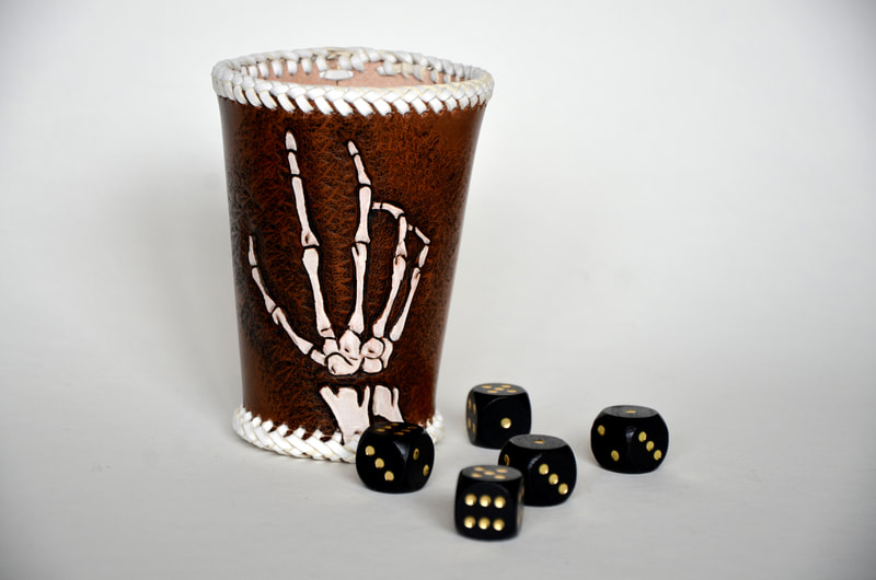 Würfelbecher aus Leder mit Skeletthand Punzierung und weissem Flechtband umflochten.